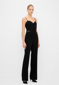 Conjunto de dos piezas negro que incluye un top corto ajustado con tirantes finos y pantalones de pierna ancha de tiro alto, complementado con tacones negros brillantes.