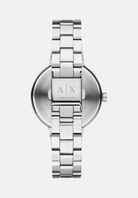 Hõbedane metalli linkkellakett, millel on klamber, millel on graveering "A|X Armani Exchange". Ümar kella nägu ja külgmine kroon on nähtavad valge tausta taustal.