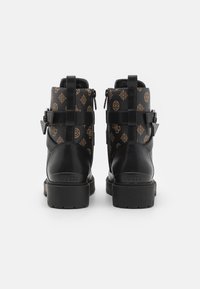 Schwarz-braune Knöchelstiefel mit gemustertem Stoff, ausgestattet mit Schnallen, einer strukturierten Oberfläche und Gummisohlen. Logo auf der Rückseite geprägt.