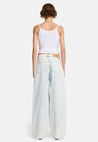 Helle blaue, weit geschnittene Jeans mit hoher Taille, ausgestattet mit einem natürlichen Lederpatch auf der Rückseite und subtilen Verblassungen im gesamten Stoff.