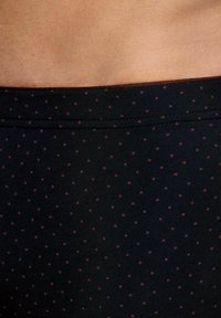 Primer plano de una cintura con tela negra con pequeños lunares rojos y piel visible por encima del cinturón.