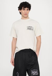 T-shirt crème à manches courtes avec un motif graphique noir sur la poitrine, associé à un short en mesh noir avec des accents brodés.