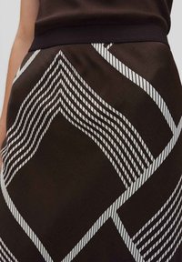 Gonna marrone con un motivo geometrico, caratterizzata da linee bianche che formano zigzag e forme di diamante; cintura elastica per una vestibilità flessibile.