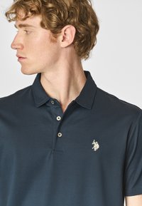 Polo shirt blu navy in cotone con apertura a due bottoni, maniche corte e piccolo logo ricamato sul petto sinistro.