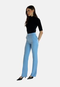 Zwarte kortoes mouwtop gecombineerd met lichtblauwe high-waisted broek met riemlussen, plooien en een rechte pijp. Zwarte puntige schoenen.