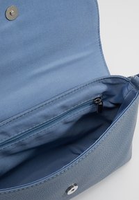 Borsa a mano azzurro chiaro con superficie texturizzata, chiusura a scatto e tasca interna con zip. Fodera in tessuto morbido. Design semplice e funzionale.