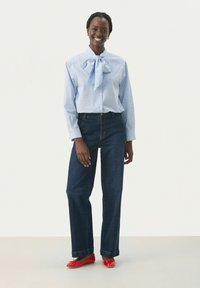 Lyseblå skjorte med knaplukning og butterfly-krave, parret med mørkeblå vide jeans og røde flade sko. Glat tekstur, afslappet design.