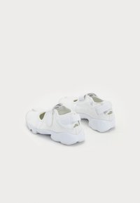 White athletic shoes with a textured upper, open sides, adjustable Velcro strap, and a cushioned, rounded sole.