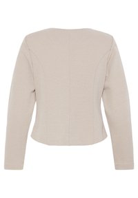 Blazer beige pour femme, sur mesure, avec manches longues, coutures arrière ajustées et ourlet légèrement raccourci.