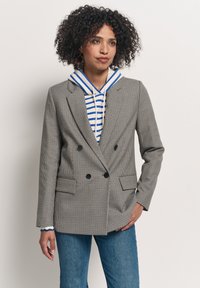 Szary, kraciasty, dwurzędowy żakiet z czarnymi guzikami i dwoma przednimi kieszeniami, nałożony na niebiesko-białą, paskowaną bluzę z kapturem. Dżinsy.