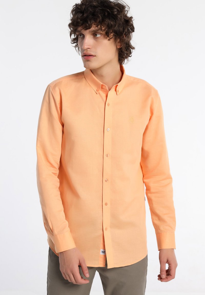 Chemise à boutons orange clair avec manches longues, poche poitrine unique et logo brodé. Le tissu semble lisse avec une légère texture.