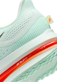 Sneaker with a mint green mesh upper, white accents, and an orange Air Zoom midsole. The textured sole features a geometric pattern for traction.