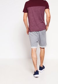 Kortärmad t-shirt för män i vinröd och grå med en färgblockdesign, kombinerad med grå shorts med rullade avslut och marinblå sneakers.