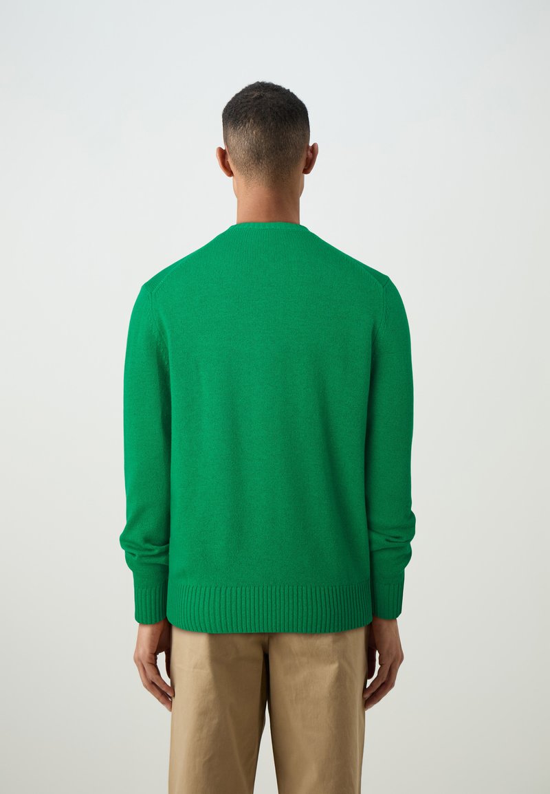 Maglione verde a maglia con scollatura rotonda, polsini e orlo a coste. La parte posteriore presenta una superficie liscia e un design aderente, abbinato a pantaloni beige.