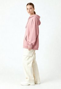 Felpa rosa oversize con tasca a marsupio e polsini a coste, abbinata a pantaloni cargo crema dal taglio morbido e sneakers bianche.