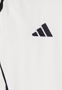 Hvid atletisk stof med et fremtrædende sort broderet tre-stribe logo. Glat tekstur med sorte accenter langs kanterne.