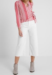 Rosa und weiße gestreifte Wickelbluse mit langen Ärmeln, kombiniert mit weißen, cropped Hosen und verzierten beigen Stiefeletten.