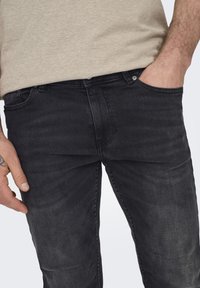 Jeans de mezclilla negra con corte slim, que cuentan con cinco bolsillos, desgastes sutiles y un cierre clásico de botón y cremallera.