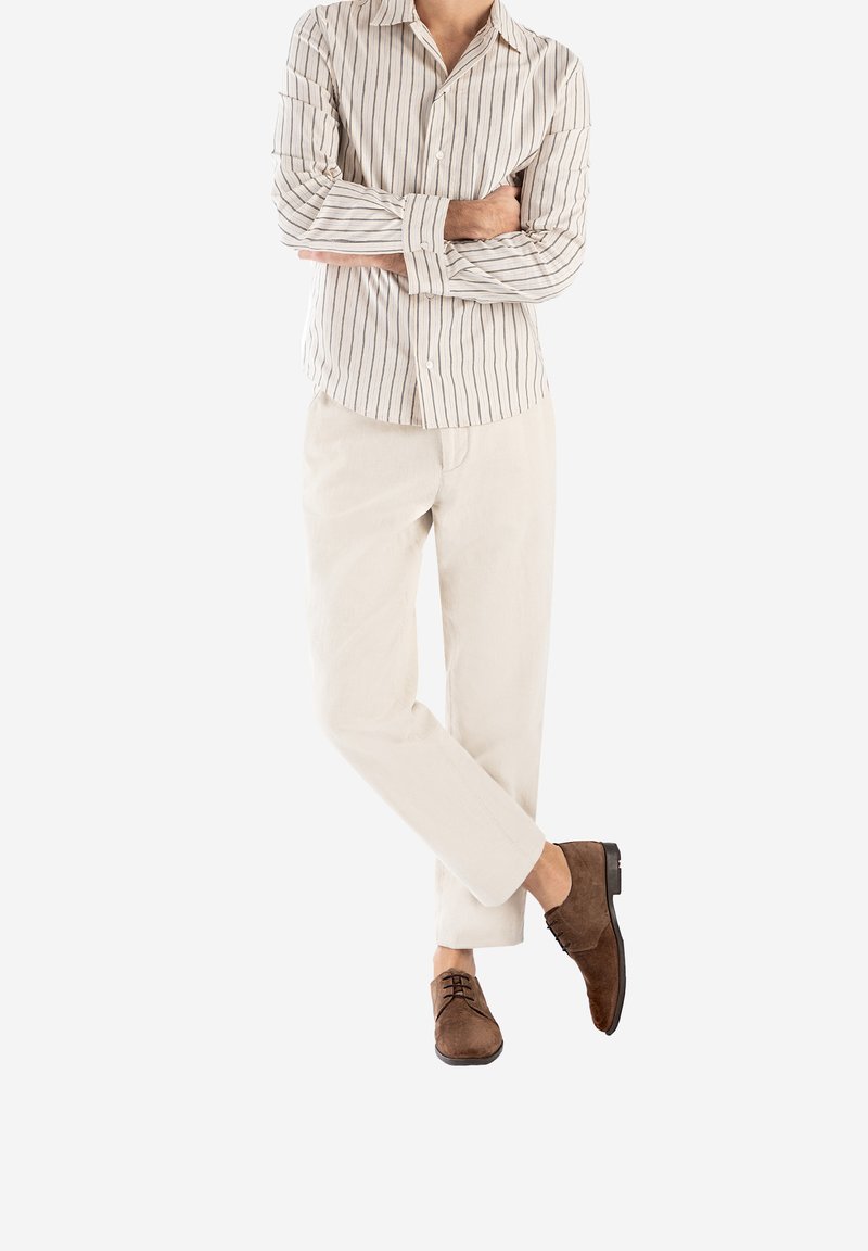 Chemise rayée à manches longues en beige et marine, associée à un pantalon beige et des chaussures en daim marron, arborant un design épuré et une coupe ajustée.
