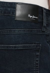 Zadné vrecko tmavomodrých džínsov s čiernou koženou etikietou Pepe Jeans London prišitou nad vreckom.