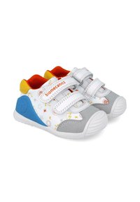 Scarpe per bambini bianche e grigie con cinturini in velcro, caratterizzate da colorati motivi di stelle e fulmini, dettagli arancioni e supporto per il tallone blu.