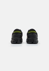 Black athletic sneakers with a textured sole, featuring a smooth upper, rounded shape, and reflective accents in neon yellow and purple.