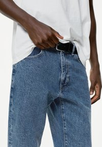 Jeans in denim blu chiaro con una trama sbiadita. Presentano cinque tasche, un passante per la cintura e cuciture a contrasto. Abbinati a una maglietta bianca.