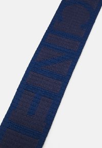Cinturino in tessuto blu navy con motivo intrecciato testurizzato e scritte blu a contrasto. Forma rettangolare con una finitura liscia.