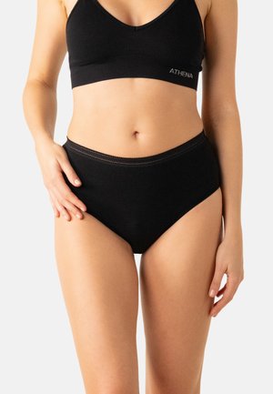 Femme portant des sous-vêtements noirs sans coutures taille haute et un soutien-gorge noir assorti avec le logo « ATHENA » sur un fond clair uni.
