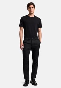 T-shirt nera, pantaloni neri slim-fit e stivali neri con lacci; tessuto morbido, design minimal, silhouette dritta con dettagli sottili.