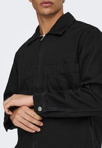 Μαύρο τζιν μπουφάν με γιακά με κουμπιά, δύο μπροστινές τσέπες και μανσέτες με κουμπιά· λείο ύφασμα με ελαφρώς άνετη εφαρμογή.