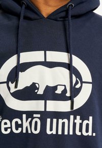 Navy hoodie with white graphic logo featuring a rhinoceros, contrasting text "eckō unltd." Soft fabric, adjustable drawstrings with metal tips.