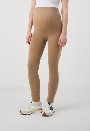 Beige ribbede leggings med høy midje, laget av et strekkbart stoff. Kombinert med hvite og brune joggesko.