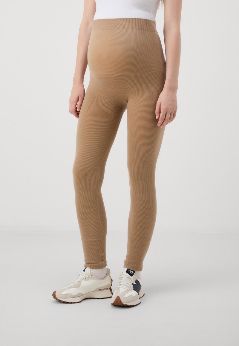 Leggings beige à côtes avec une taille haute, en tissu extensible. Associés à des chaussures de sport blanches et beiges.