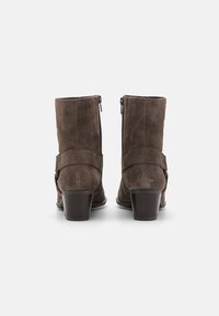 Botines de ante marrón con un acabado ligeramente texturizado, que cuentan con una cremallera trasera, una correa decorativa y un tacón grueso.