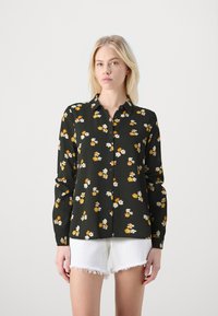 Svart blommig skjorta med orange och vita blommor, långa ärmar, knäppning fram och i ett mjukt, lätt material. Kombinerad med vita shorts.