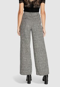 Pantaloni a gamba larga in un motivo houndstooth grigio, con vita alta, tessuto strutturato e vestibilità sartoriale. Indossate stivaletti neri con tacco quadrato.
