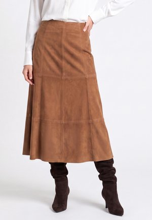 Donna che indossa una gonna midi a-line in camoscio marrone abbinata a stivali con tacco morbidi in camoscio marrone scuro e una camicia bianca a maniche lunghe.