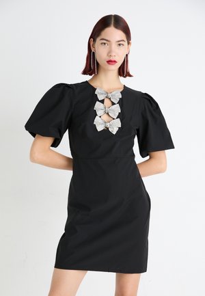 Schwarzes Kleid mit Puffärmeln und rundem Ausschnitt, das an der Vorderseite mit einem dekorativen Detail aus fünf silberfarbenen Schleifen versehen ist.