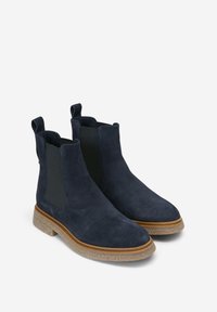 Botines de ante azul marino con paneles laterales elásticos y tiradores. Cuentan con una suela de goma texturizada y una entresuela de color marrón claro en contraste.