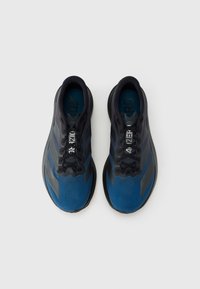 Kék és fekete sportcipők sima textúrával, áramvonalas kialakítással, hat fűzőlyukkal és márkázott talpbetét részletekkel.