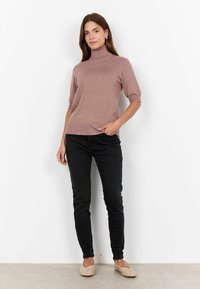 Pulover roz deschis cu guler înalt, cu mânecă scurtă, cu o formă ajustată, textură netedă, asociat cu blugi negri mulați și pantofi slip-on bej.