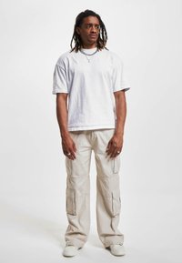 T-shirt bianco in cotone, vestibilità oversize, collo rotondo. Pantaloni cargo beige con più tasche e silhouette rilassata. Sneakers bianche. Collana semplice a catena.