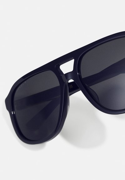 Lunettes de soleil en plastique navy avec des verres foncés, présentant un design audacieux et des découpes dans la monture.