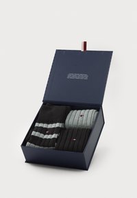 Set of four cotton socks in a navy box. Includes solid black, light gray, dark gray ribbed, and dark gray striped designs. Red and white accents visible.