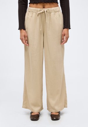 Beige Hosen mit weitem Bein, elastischem Bund und Kordelzug, kombiniert mit dunkelbraunen flachen Schuhen und einem schwarzen, langärmligen Crop-Top.
