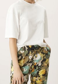 Biały bawełniany t-shirt z krótkimi rękawami w połączeniu z wzorzystymi, wielokolorowymi spodniami z kwiatowymi wzorami w kolorach zielonym, żółtym i czarnym.