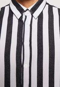 Zwart-witte gestreepte shirt met een button-down kraag, voorzien van verticale strepen, zacht materiaal en witte knopen langs de sluiting.