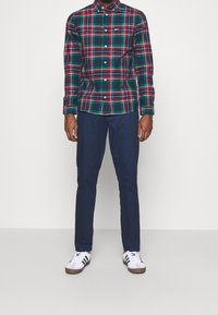 Camisa de cuadros en verde, rojo y azul marino, combinada con pantalones azul marino y zapatillas blancas. Presenta un cuello con solapa y mangas largas.