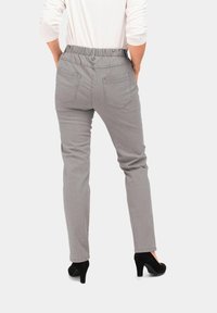 Graue Hose mit elastischem Bund, ausgestattet mit zwei Gesäßtaschen und geradem Beinschnitt. Getragen mit schwarzen High Heels.